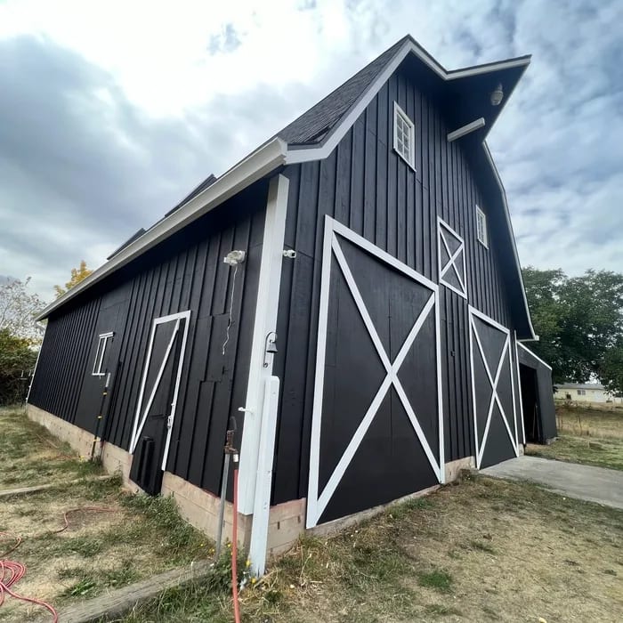 Completed matte black gambrel barn with crisp white trim and X doors
